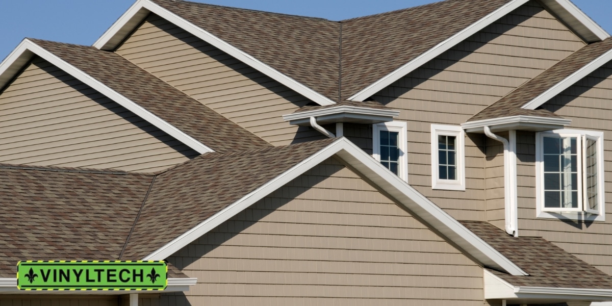 Close-up of a modern home with beige vinyl siding and a multi-gabled roof, featuring clean white trim and well-maintained shingles, with the Vinyltech logo in the bottom left corner.