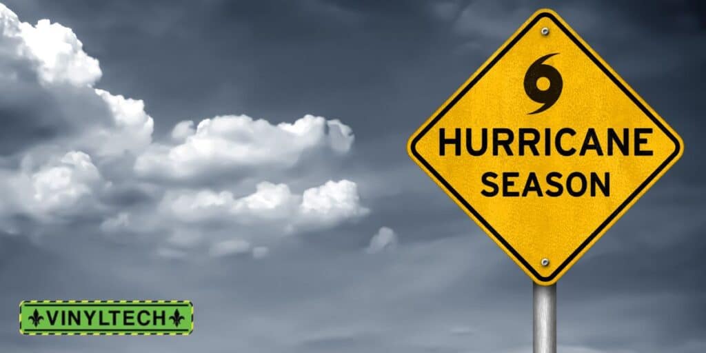 Yellow warning sign with the text 'Hurricane Season' and a hurricane symbol, set against a cloudy gray sky. The Vinyltech logo appears in the bottom left corner.