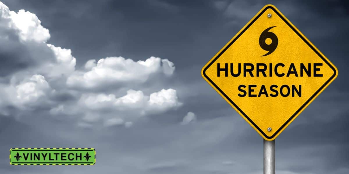 Yellow warning sign with the text 'Hurricane Season' and a hurricane symbol, set against a cloudy gray sky. The Vinyltech logo appears in the bottom left corner.