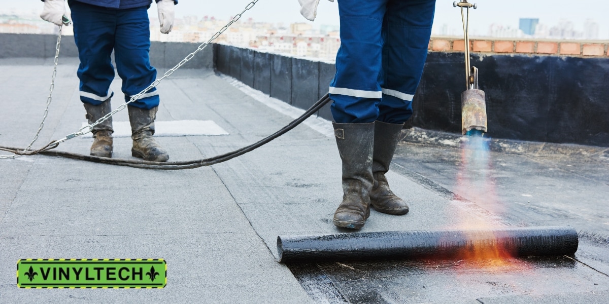 Roofers installing a torch-down flat roofing system using heat application, demonstrating the durability and water resistance of this commercial roofing solution, with the Vinyltech logo.