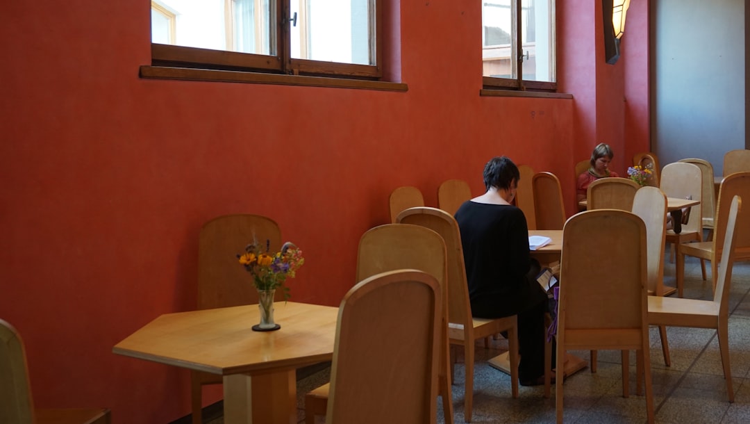 A homeowner sitting at a kitchen table with a laptop, looking thoughtfully at insurance documents and paperwork related to a storm damage claim.