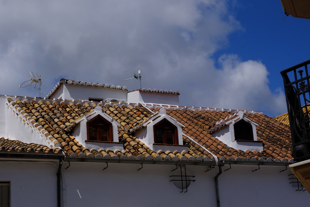 A professional roofer carefully examining old, curling, or missing asphalt shingles on a residential roof, signifying the inspection process.