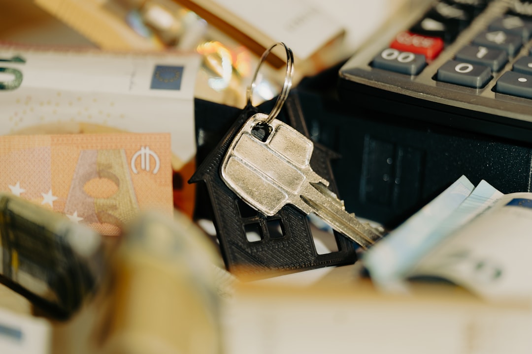 Person sits at a modern desk, thoughtfully using a calculator with a set of house keys nearby, representing the financial ...