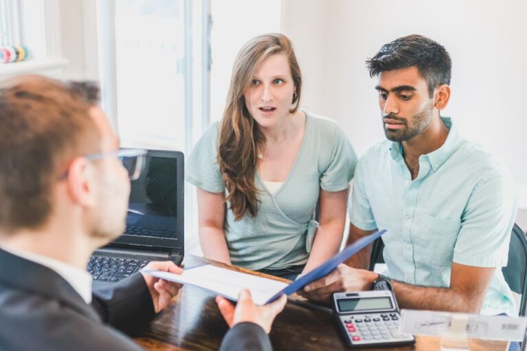 Couple sits at a dining table with a laptop and papers, seriously discussing their finances for a new home in a bright, mo...